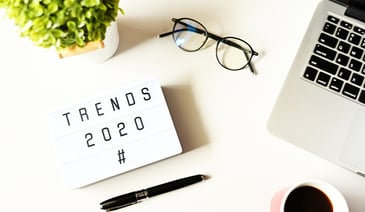 Notepad with text that says Trends 2020 next to macbook and eyeglasses 