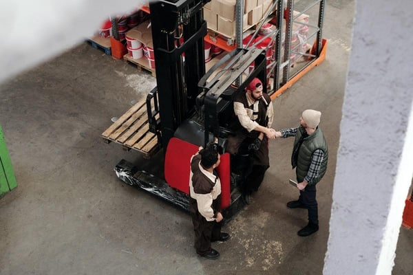 3 Warehouse employees shaking hands next to red forklift - aerial view