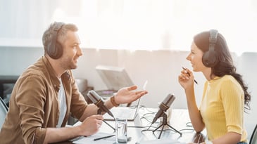 two radio hosts in headphones talking while recording podcast in radio studio
